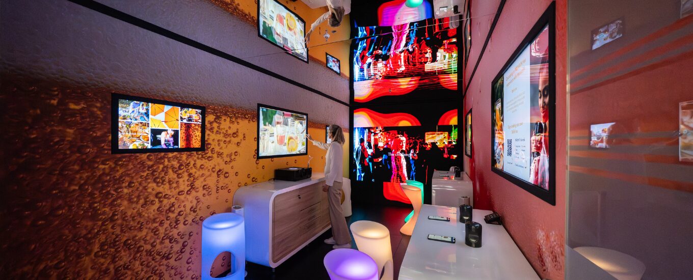A bright and colourful immersive room featured within the Givaudan booth at Drinktec 2025 where a person is using the tv to explore