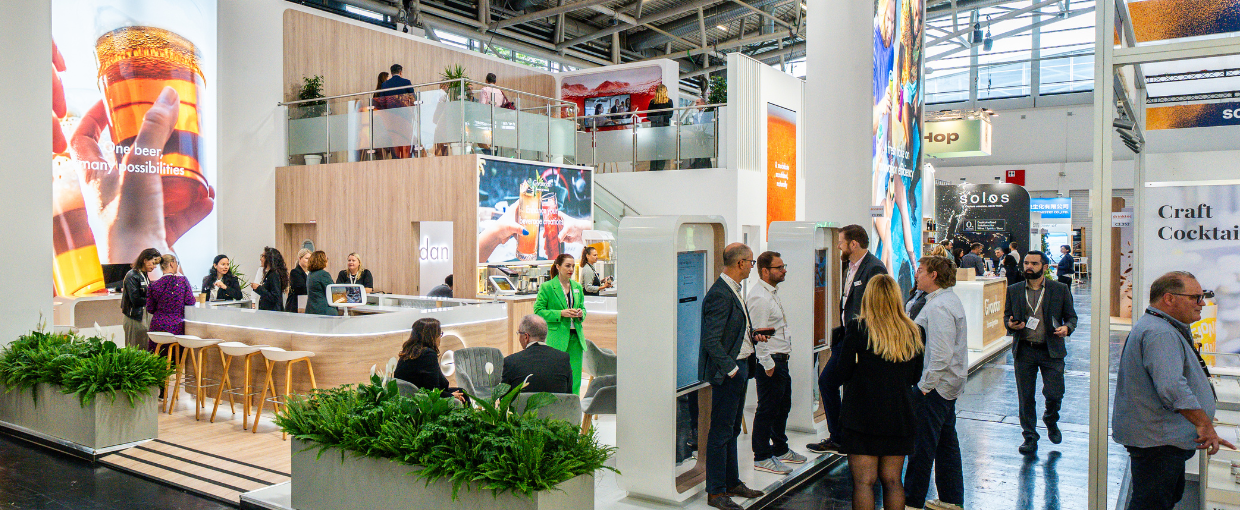 A banner of the Givaudan booth at Drinktec where there is a wide view of the booth showing large graphics, upstairs bar and people on the booth chatting