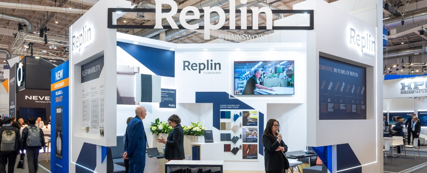 Replin booth at AIX 2025 front shot of the booth with large commercial signage to the top and multiple visitors chatting over the reception counter
